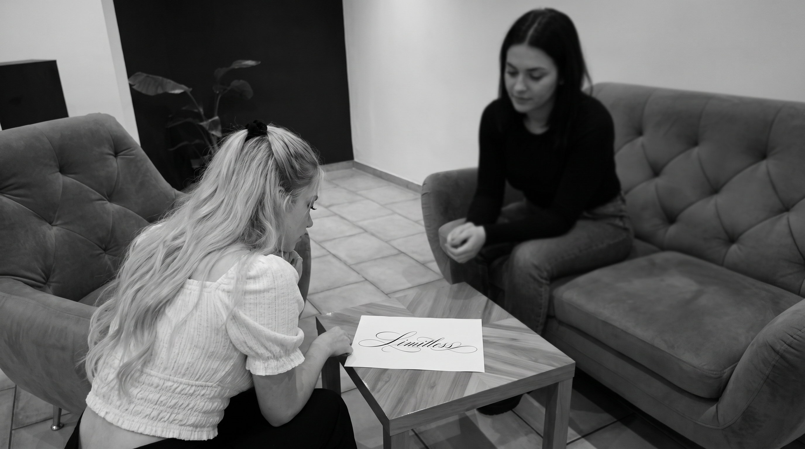 Beratung im Studio: ein Fineline Schriftzug-Entwurf liegt auf dem Tisch, Schwarz-Weiß-Aufnahme